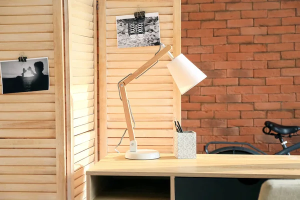 Modern lamp and folding screen near brick wall