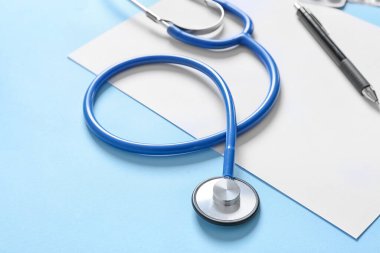 Modern stethoscope and sheet of paper on color background, closeup