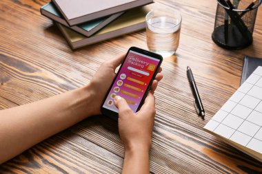 Female hands and mobile phone with open page of delivery service application on table