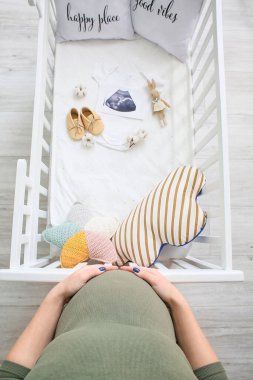 Pregnant woman near crib with sonogram image and baby accessories