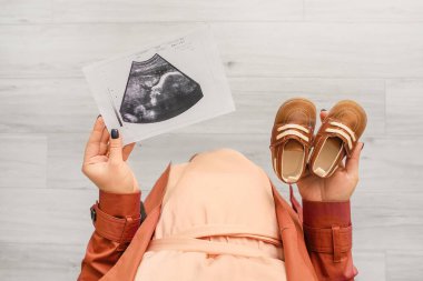 Pregnant woman with baby booties and sonogram image at home, closeup