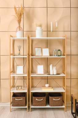 Shelf unit with blank photo frames and decor near color wall in room