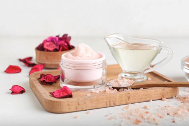 Vücut fırçası kavanozu, temel yağ, deniz tuzu ve çiçek yapraklarıyla hafif arkaplanda bileşim