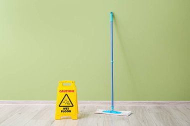 Floor mop and caution sign near color wall