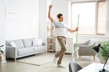 Young man listening to music while mopping floor in living room