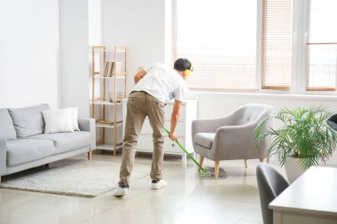 Young man listening to music while mopping floor in living room