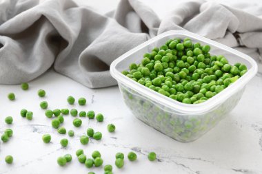 Plastic container with green peas on light background, closeup
