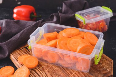 Plastic containers with carrot on dark background, closeup