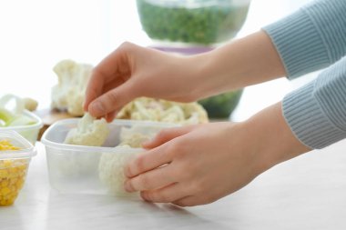 Kadın karnabaharı mutfaktaki plastik kutuya koyuyor, yakın plan.