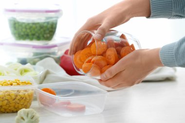Kadın mutfaktaki plastik kabın içine havuç koyuyor.