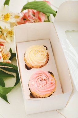 Lezzetli kekler ve açık arkaplanda çiçekler olan bir kutu.