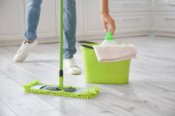 Young man mopping floor in kitchen