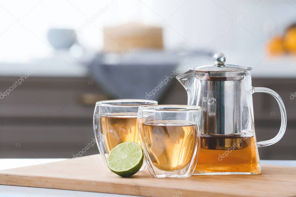 Teapot, glasses with hot tea and lime on table in kitchen