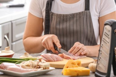 Woman cutting chicken fillet in kitchen
