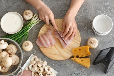Woman cutting chicken fillet on grey background