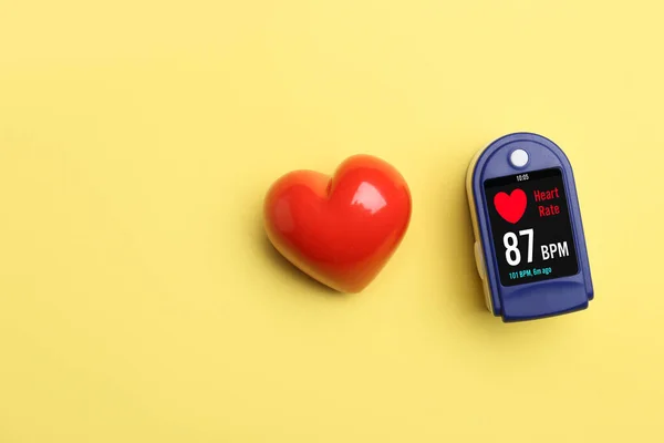 Red heart and pulse oximeter on color background