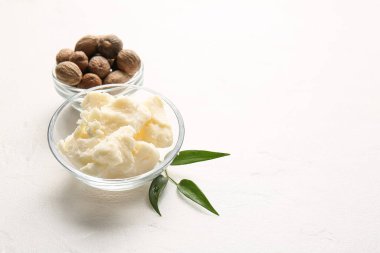 Bowls with shea butter and nuts on light background