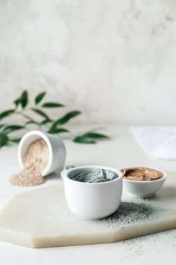 Bowls with cosmetic clay on light background