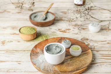 Plate with different cosmetic clay on light wooden background