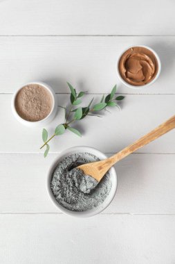 Bowls with cosmetic clay on light wooden background