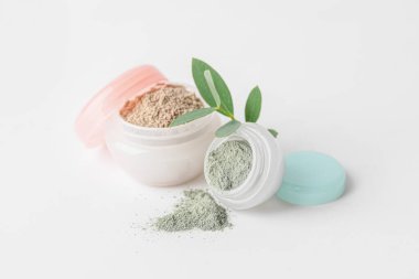 Jars with cosmetic clay on white background