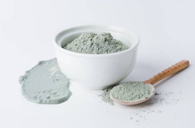 Bowl and spoon with cosmetic clay on white background