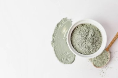 Bowl and spoon with cosmetic clay on white background