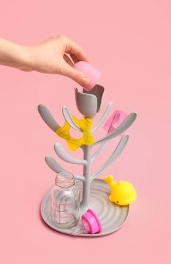 Female hand and drying rack for baby bottles on color background