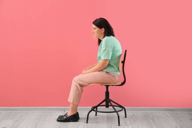 Woman with bad posture sitting on chair near color wall
