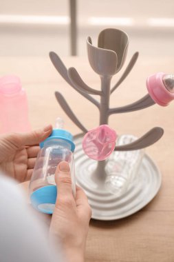 Woman with drying rack for baby bottles on table at home