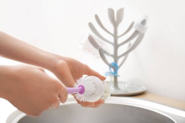 Kadın evde bebek şişesini temizliyor.