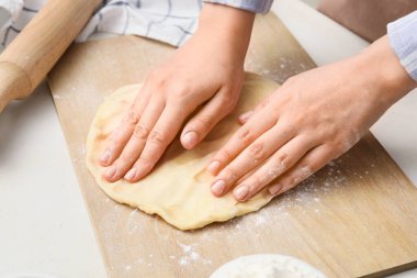 Woman kneading dough on board in kitchen, closeup