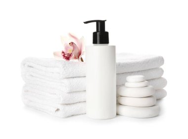 Stack of clean towels, stones and bottle of cosmetic product on white background