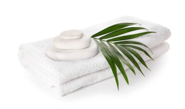Clean towels, spa stones and palm leaf on white background