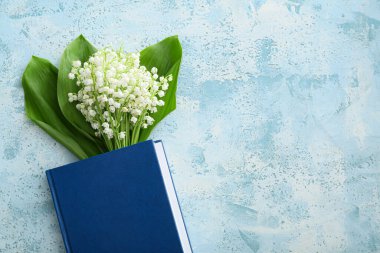 Beautiful lily-of-the-valley flowers and book on color background