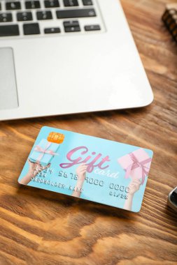Tahta arka planda hediye kartı ve dizüstü bilgisayar, yakın plan.