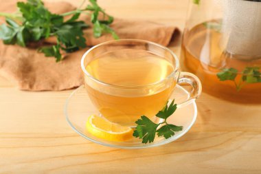 Çaydanlık ve bir fincan sıcak çay, ahşap arka planda maydanoz ve limon.