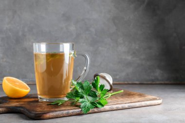 Bir fincan sıcak çay, maydanoz ve arkaplanda limon.