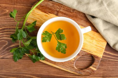 Tahta arka planda bir fincan sıcak çay ve maydanoz.