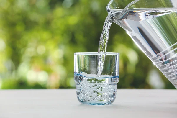 Pouring fresh water from jar into glass on table outdoors, closeup