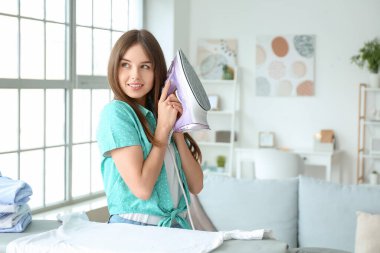 Evde çamaşırları ütüleyen genç bir kadın.