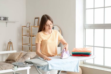 Evde çamaşırları ütüleyen genç bir kadın.