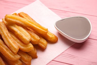 Lezzetli churros ve erimiş çikolata soslu parşömen, ahşap kaplama, yakın plan.