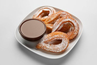 Hafif arka planda lezzetli churros ve erimiş çikolata soslu tabak, yakın plan.