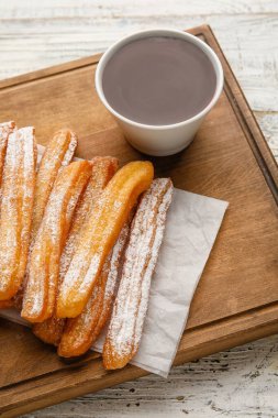 Yumuşak ahşap arka planda lezzetli churros ve erimiş çikolata soslu tahta, yakın plan.