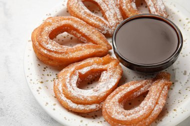 Hafif arka planda lezzetli churros ve erimiş çikolata soslu tabak, yakın plan.
