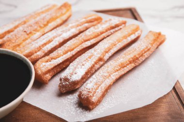 Hafif arka planda lezzetli churros ve erimiş çikolata soslu pano, yakın plan.