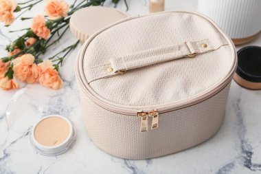 Dekoratif kozmetik ürünleri ve hafif arka planda çiçekleri olan şık bir çanta.