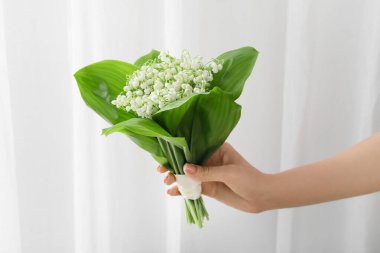 Işıklı arka planda vadideki güzel çiçekleri olan kadın eli.