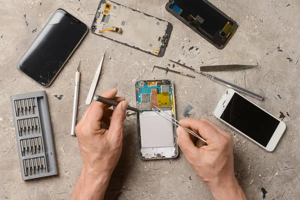 Male technician repairing damaged mobile phone on grunge background